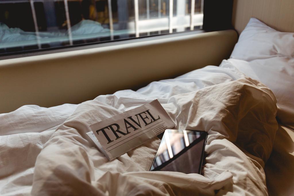 κλείνω πάνω θέα του ταξίδια εφημερίδα και tablet στο κρεβάτι στο δωμάτιο του ξενοδοχείου - Φωτογραφία, εικόνα