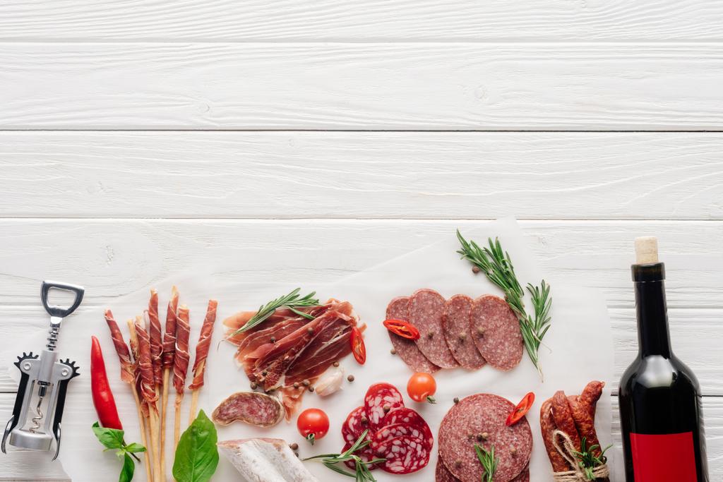 flat lay with bottle of red wine, bottle opener and meat snacks on wooden surface - Photo, Image