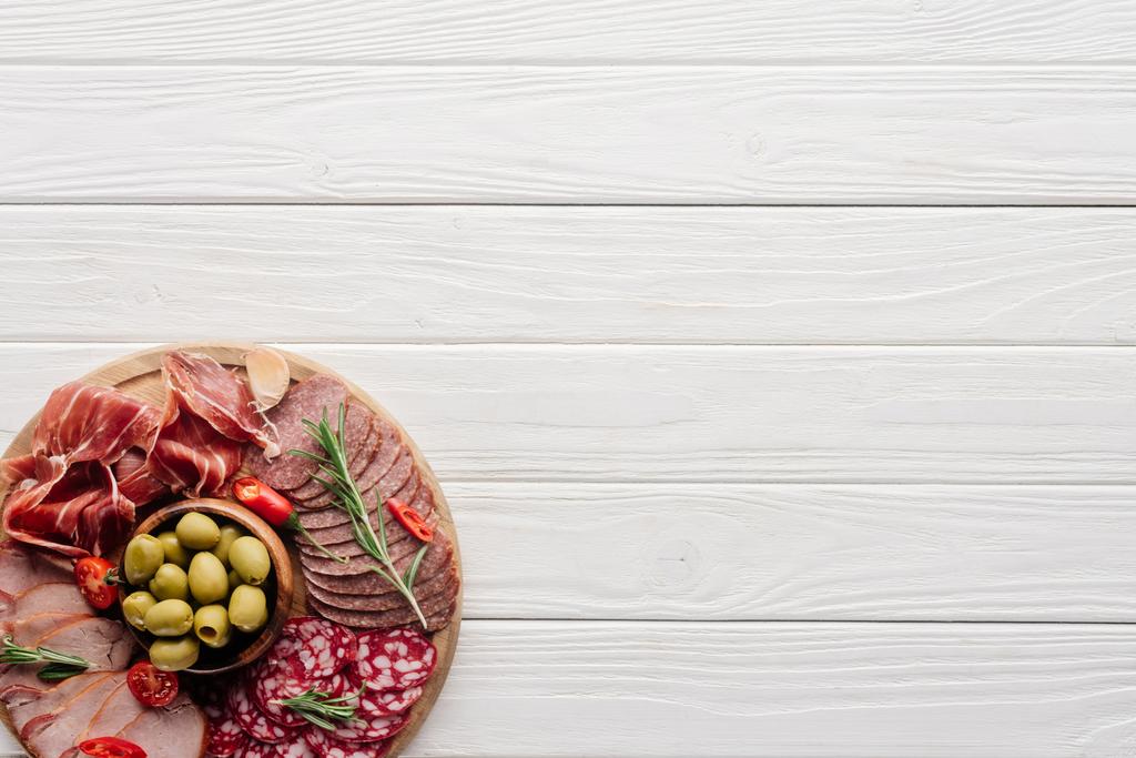 pohled shora uspořádání různé pochutiny z masa a olivy na bílé dřevěné pozadí - Fotografie, Obrázek