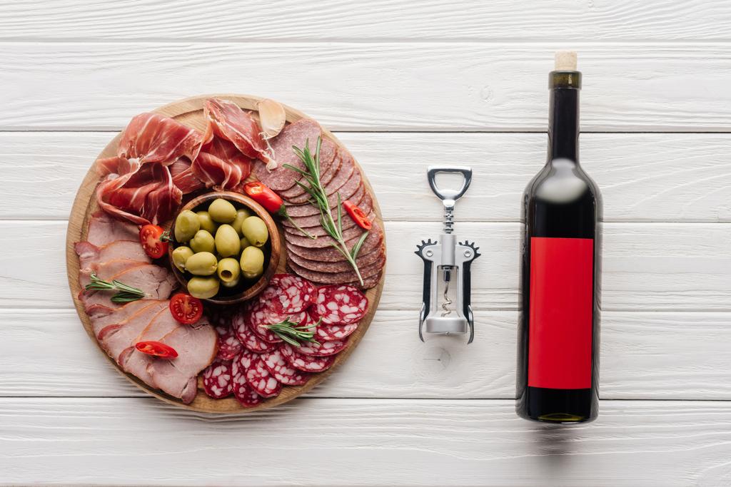 acostado plano con botella de vino tinto, abrebotellas y aperitivos de carne en la superficie de madera
 - Foto, imagen
