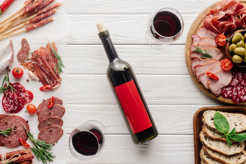 composition alimentaire avec bouteille et verres de vin rouge, morceaux de pain, olives et collations à la viande sur plateau en bois blanc
 - Photo, image