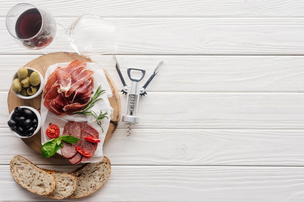 vlakke leggen met glas rode wijn, stukken van brood en diverse vlees snacks op witte houten tafelblad - Foto, afbeelding