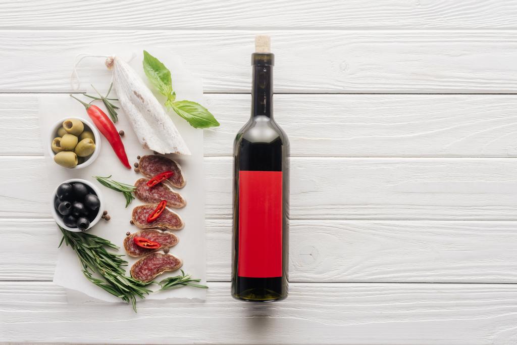 şişe kırmızı şarap ve çeşitli et aperatifler üstten görünüm üzerinde beyaz ahşap masa - Fotoğraf, Görsel