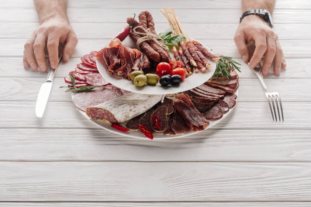 partial view of man at white wooden tabletop with various meat snacks - Photo, Image