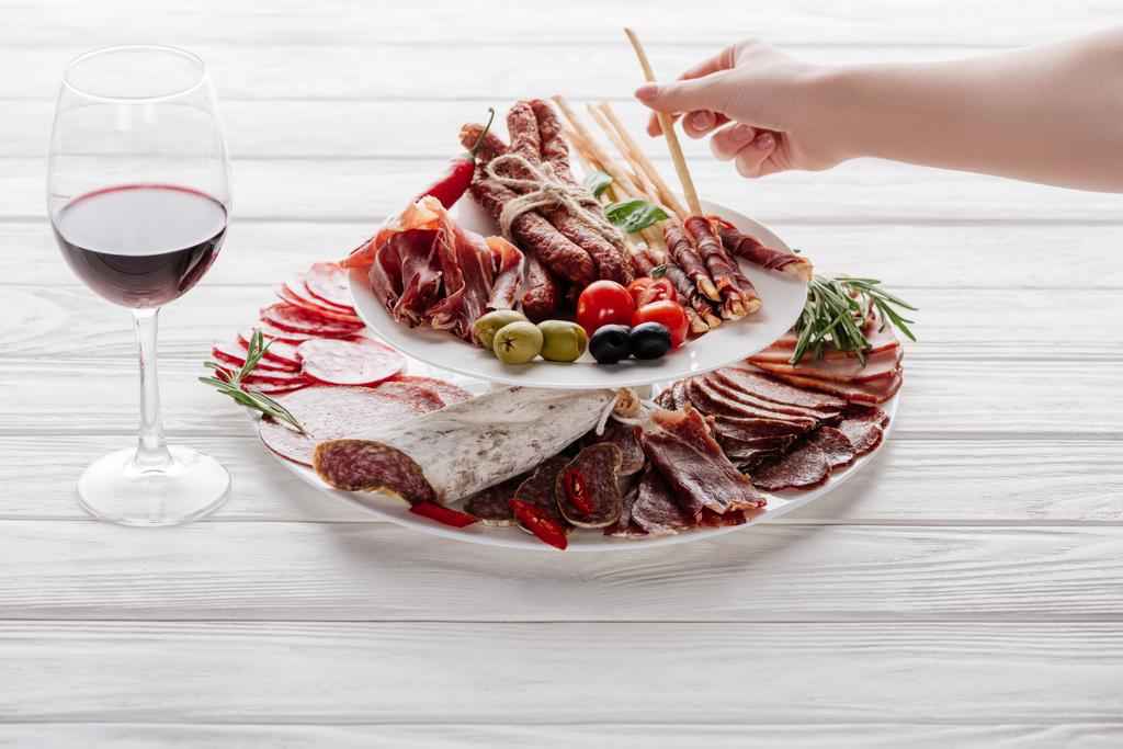 cropped shot of woman, glass of red wine and meat snacks on white wooden surface - Photo, Image