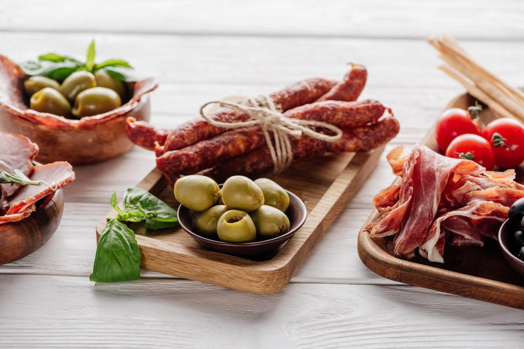 food composition with various meat appetizers, olives and basil leaves on white wooden surface - Photo, Image