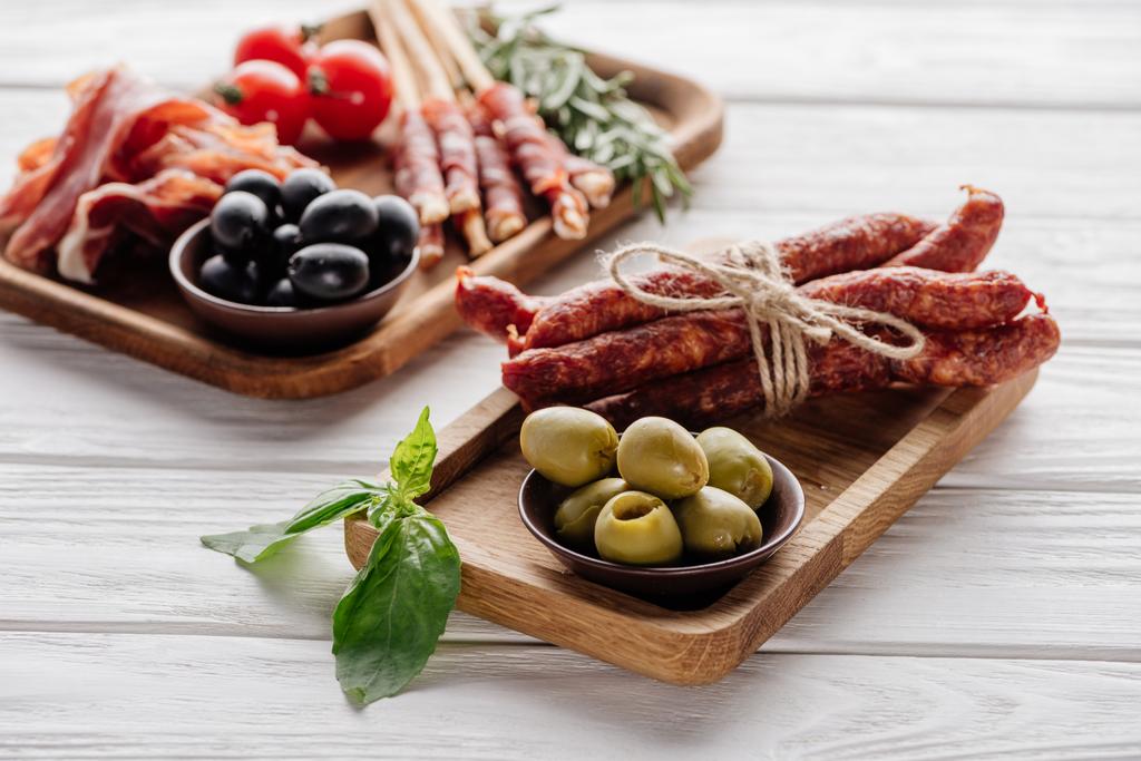composition alimentaire avec divers apéritifs à base de viande, olives et feuilles de basilic sur une surface en bois blanc
 - Photo, image