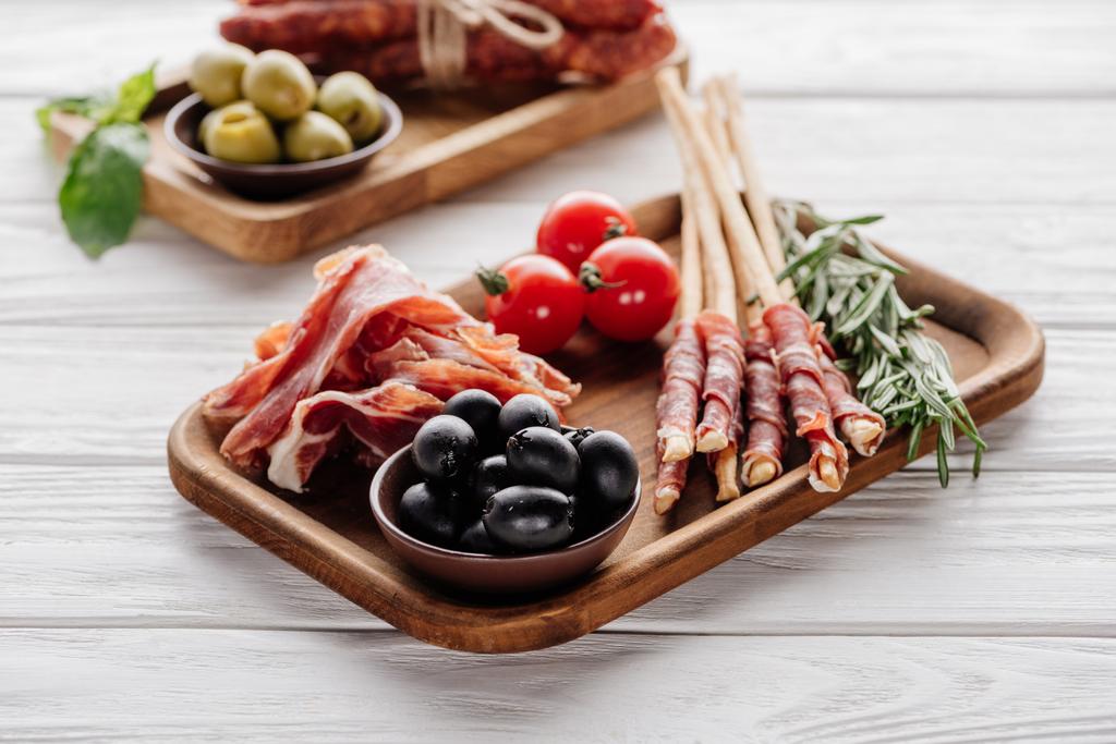 composition alimentaire avec divers apéritifs de viande, olives et romarin sur une surface en bois blanc
 - Photo, image