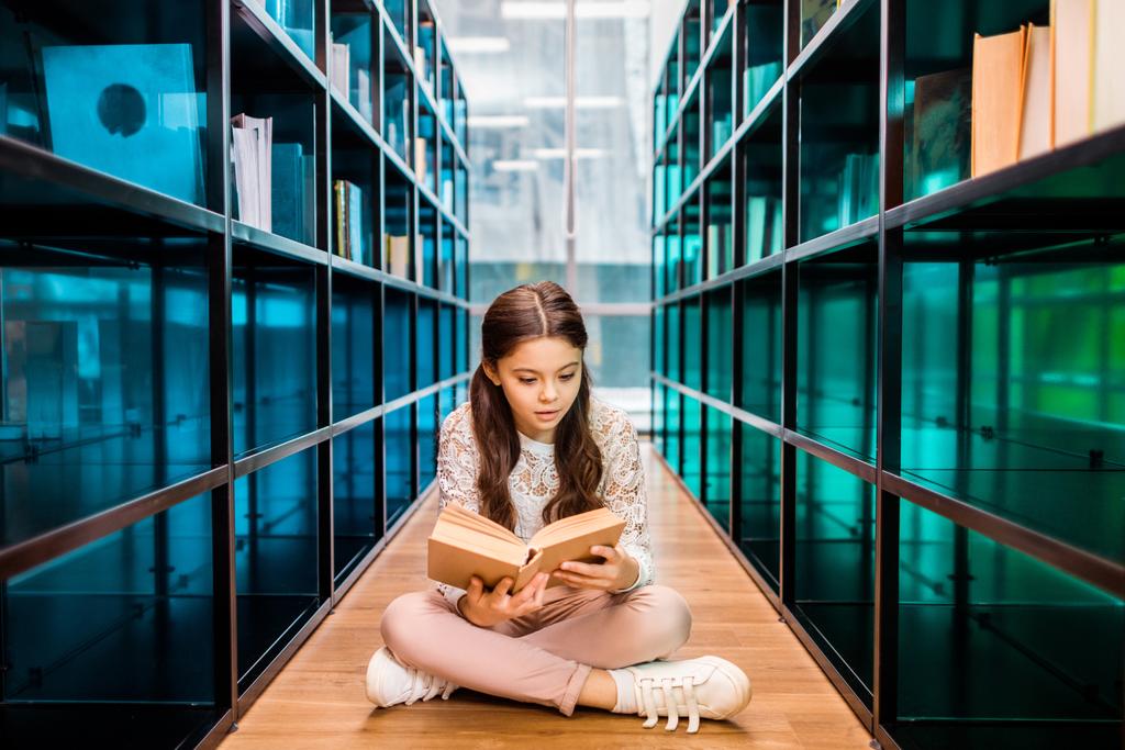 восхитительная школьница читает книгу на полу в библиотеке
 - Фото, изображение
