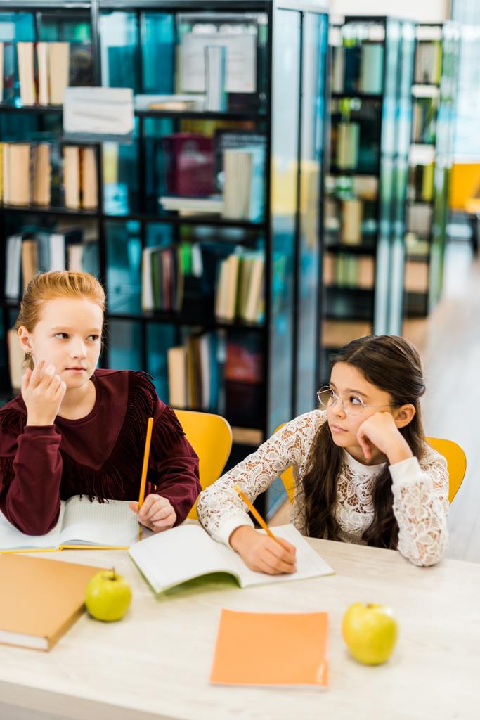 schoolgirls writing with pencils while studying in library  - Photo, Image