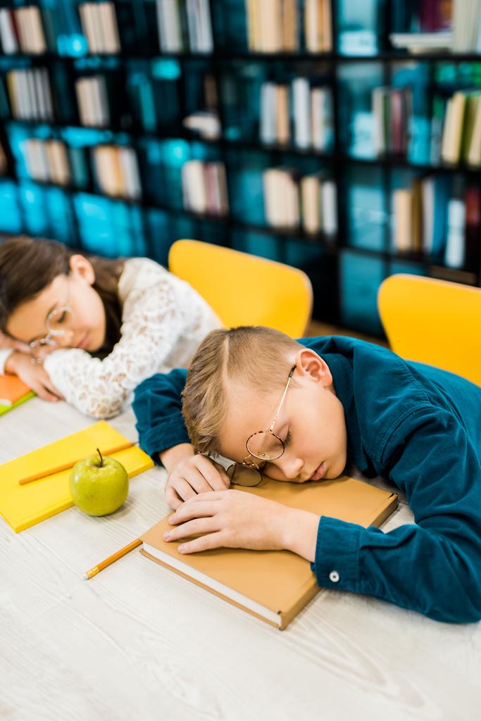 aranyos fáradt schoolkids a szemüvegek alszik a táblázat könyvek könyvtár   - Fotó, kép
