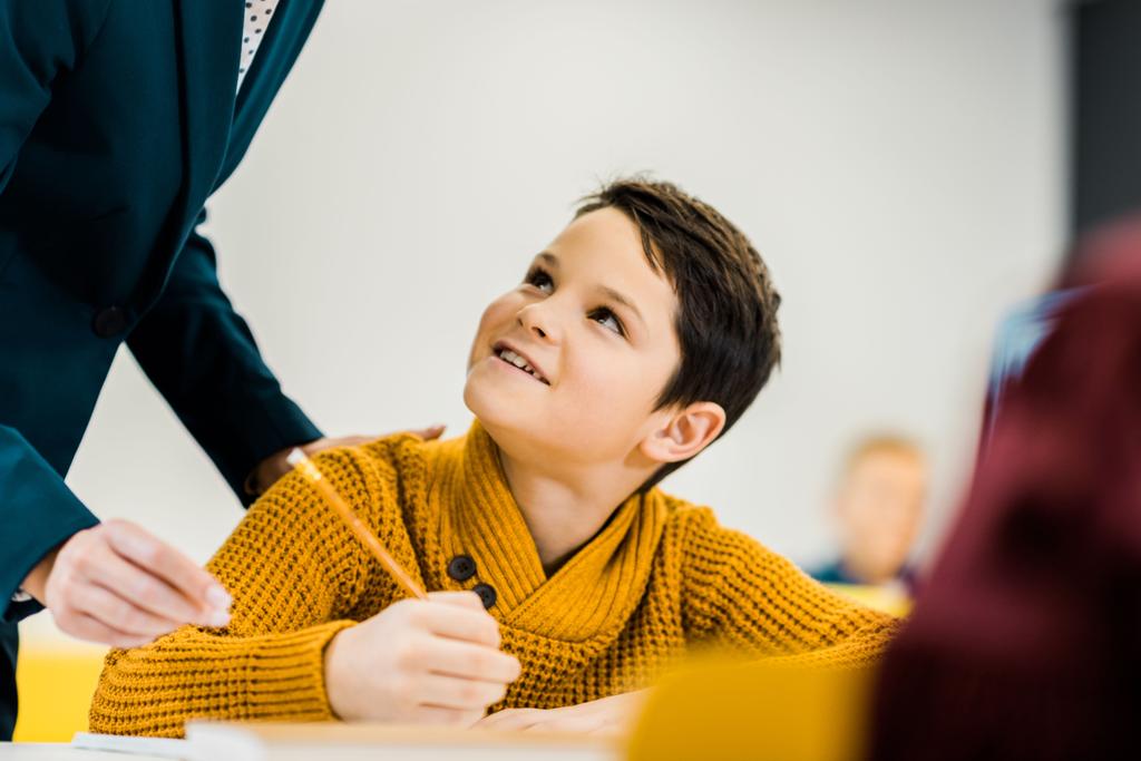 Oříznout záběr usměvavý chlapec drží tužku a při pohledu na učitele - Fotografie, Obrázek