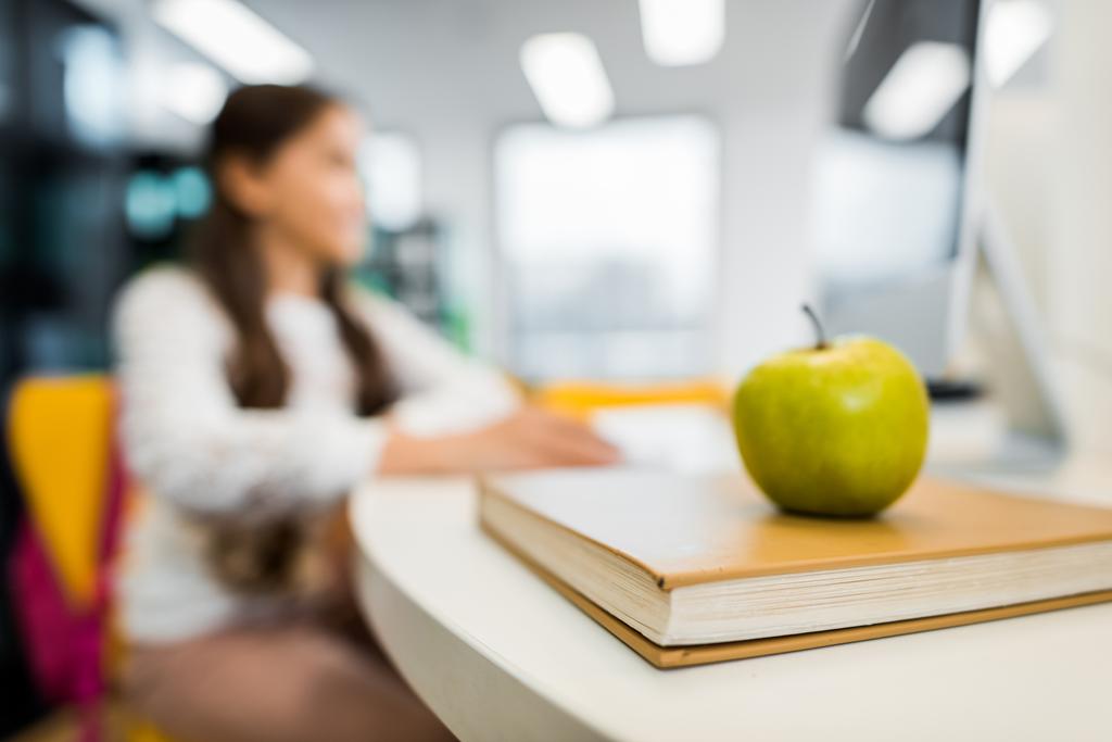 close-up view of apple on book and schoolchild sitting behind in library - Photo, Image