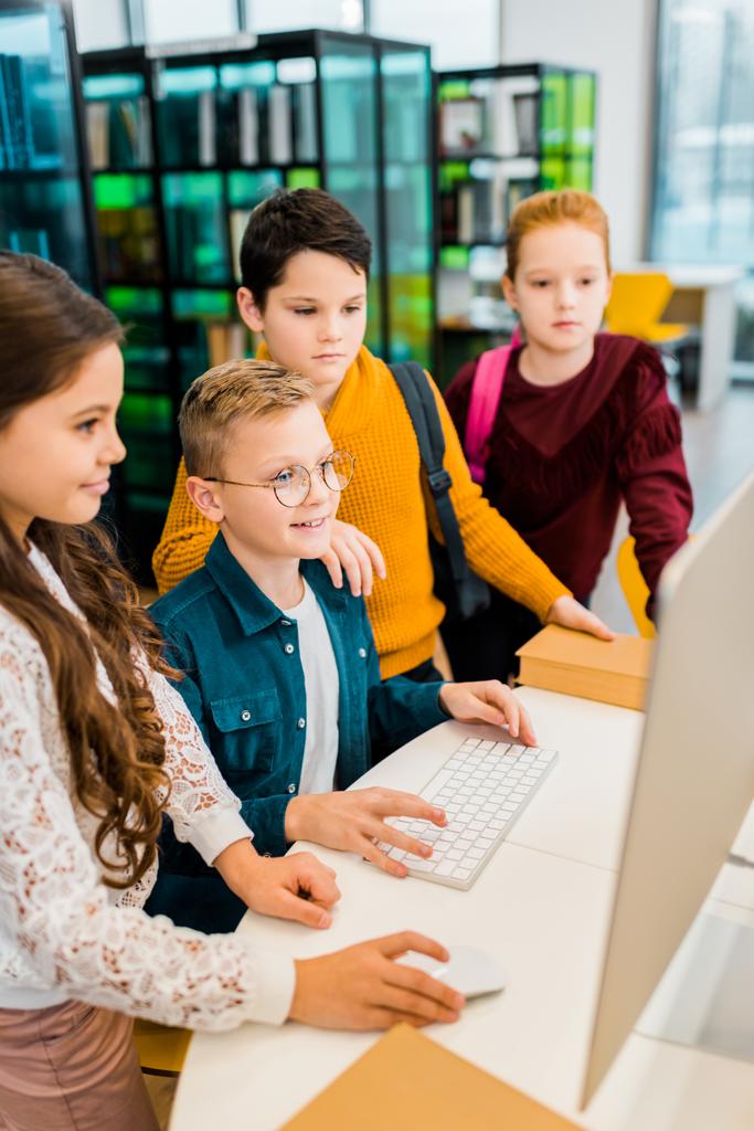 hoge hoekmening van schattige lachende schoolkinderen desktopcomputer gebruikt in bibliotheek  - Foto, afbeelding