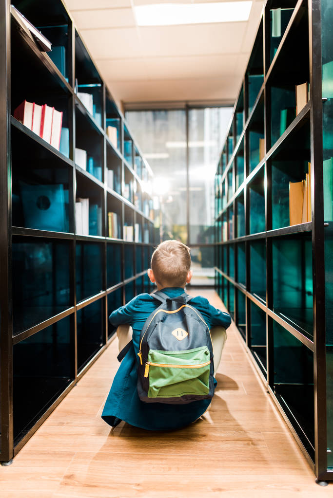 zadní pohled na školák batoh sedí na podlaze v knihovně  - Fotografie, Obrázek