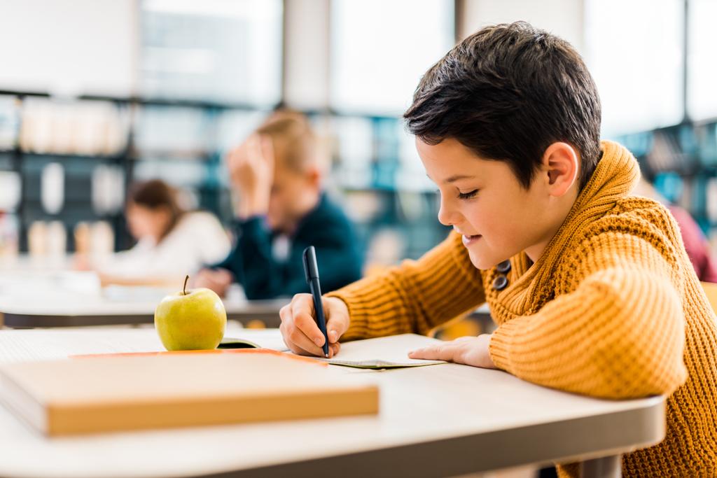 menino sorridente escrevendo com caneta enquanto estudava com colegas na biblioteca
 - Foto, Imagem