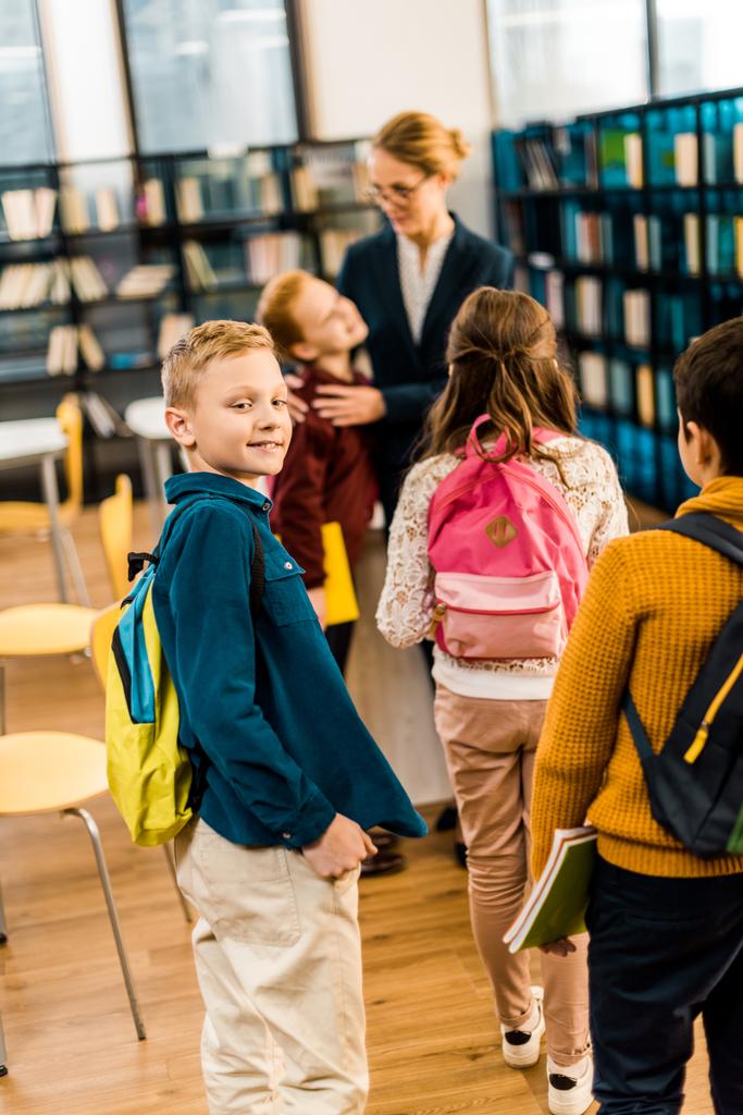 visão traseira de escolares com mochilas em pé com bibliotecário na biblioteca
 - Foto, Imagem