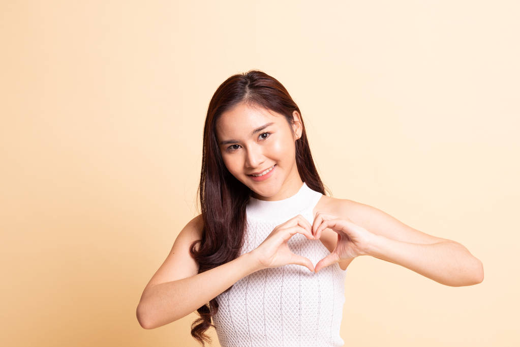 Jeune femme asiatique montrer signe de la main coeur sur fond beige - Photo, image