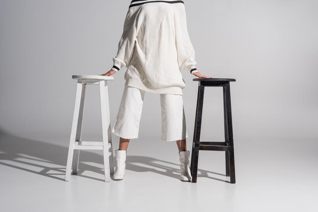 immagine ritagliata di ragazza in maglione alla moda e pantaloni in piedi tra sedie in bianco e nero su bianco
 - Foto, immagini