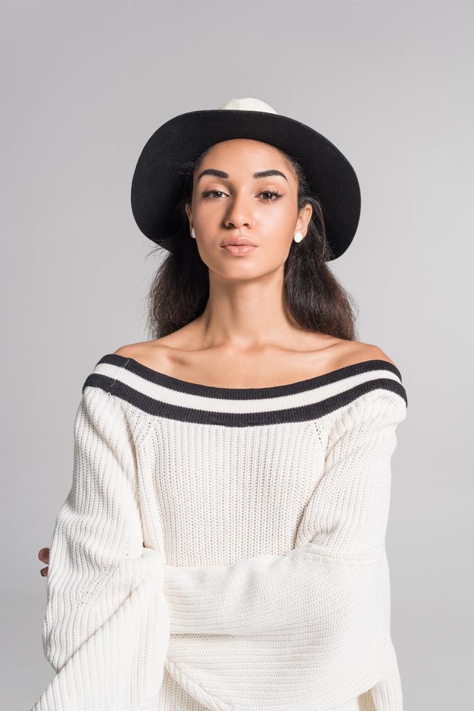 atractiva chica afroamericana en suéter blanco con estilo y sombrero mirando a la cámara aislada en blanco
 - Foto, imagen
