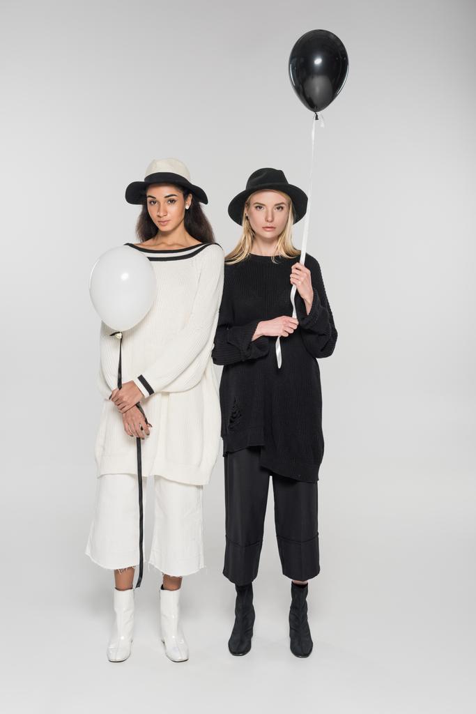 iki balon tutarak ve kameraya beyaz üzerinde seyir siyah beyaz giysili güzel çok kültürlü kadınlar - Fotoğraf, Görsel