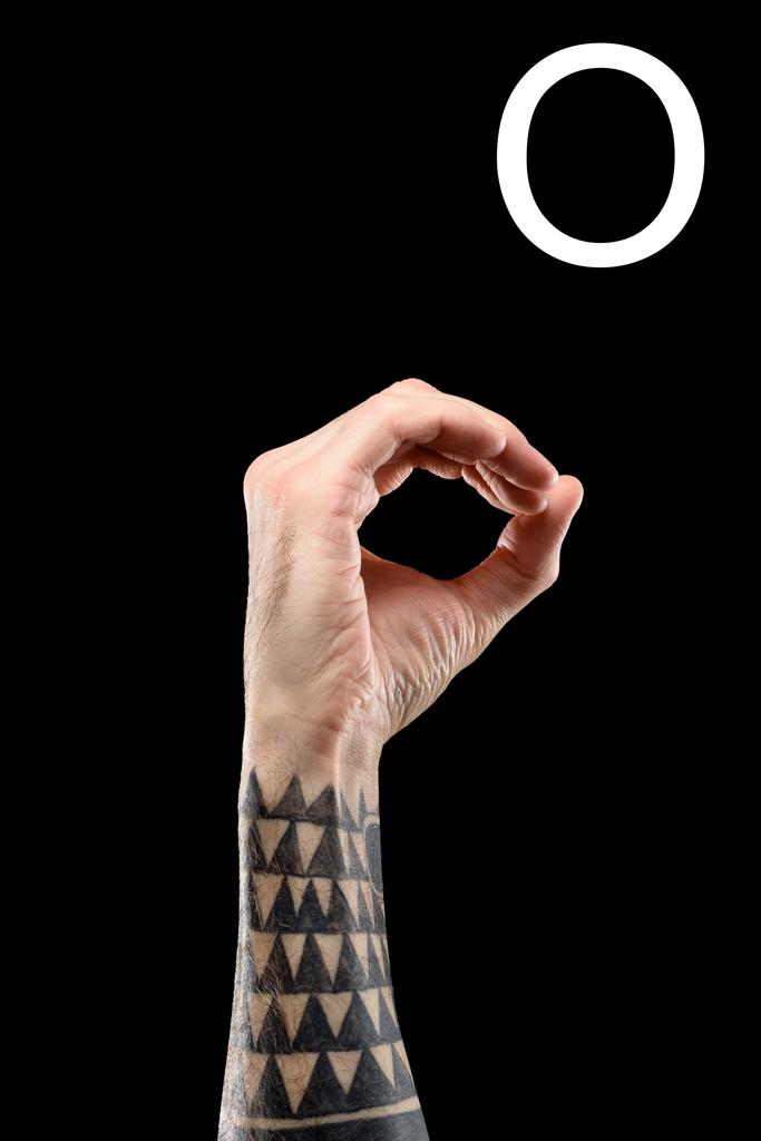 cropped view of tattooed hand showing latin letter - O, sign language, isolated on black - Photo, Image