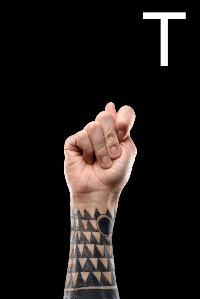 vista recortada de la mano masculina tatuada que muestra la letra latina T, lenguaje sordo y mudo, aislado en negro
 - Foto, imagen