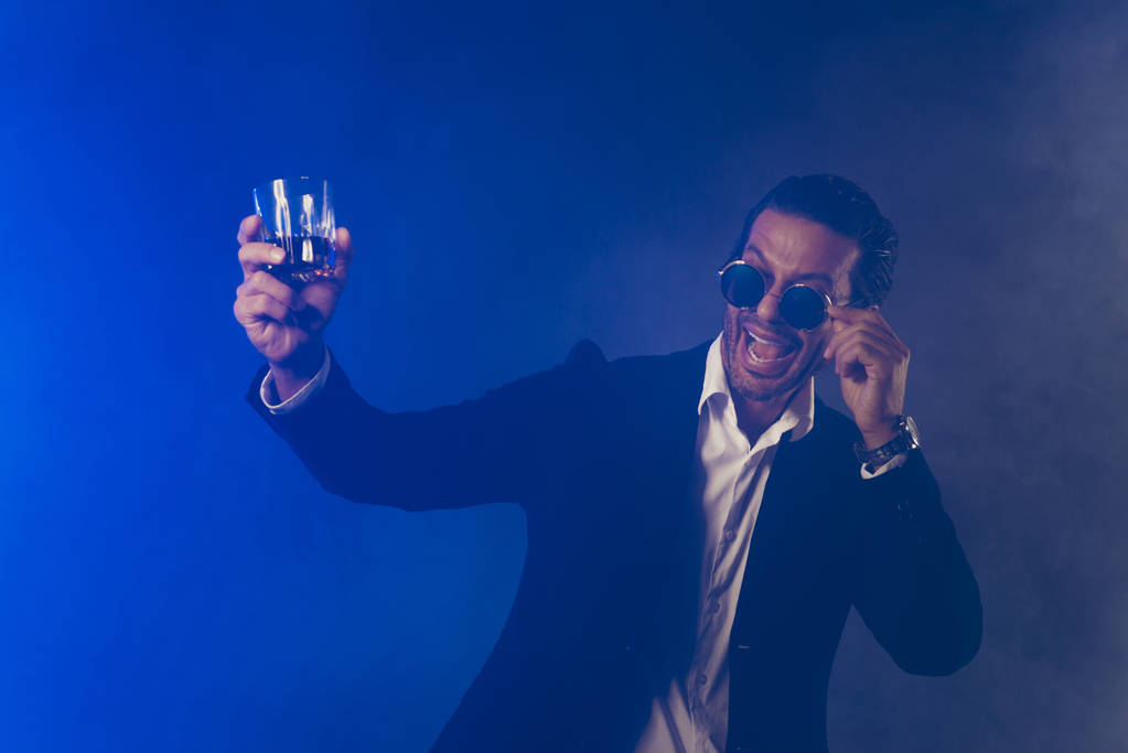 Retrato de agradável legal louco atraente bonito alegre alegre feliz homem em jaqueta preta tocando óculos óculos segurando vidro se divertindo abriu a boca isolada sobre azul escuro fumaça fumaça fundo
 - Foto, Imagem