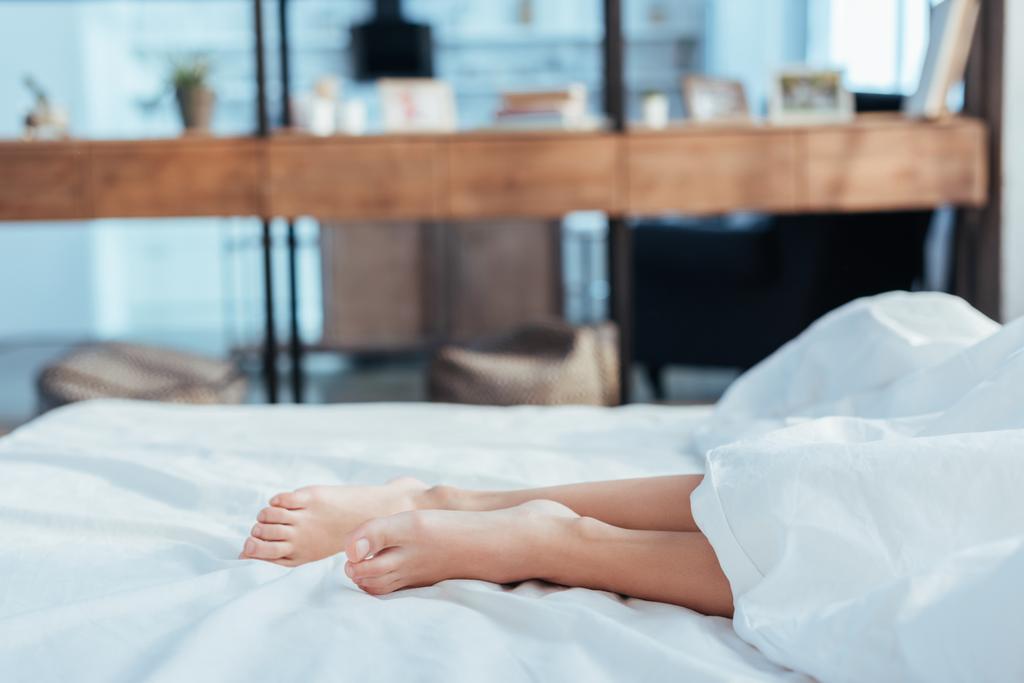 abgeschnittenes Bild weiblicher Beine unter Decke im Bett während der Morgenstunde zu Hause - Foto, Bild