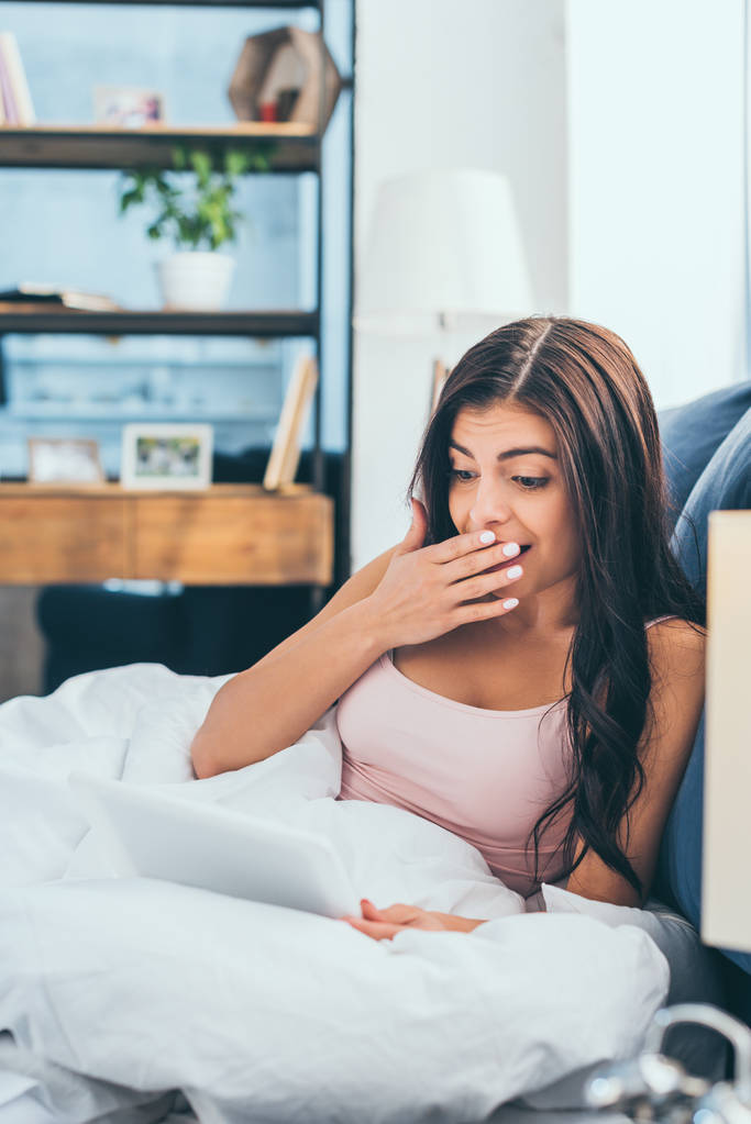 surpresa jovem mulher cobrindo a boca com a mão e usando tablet digital na cama durante o horário da manhã em casa
 - Foto, Imagem