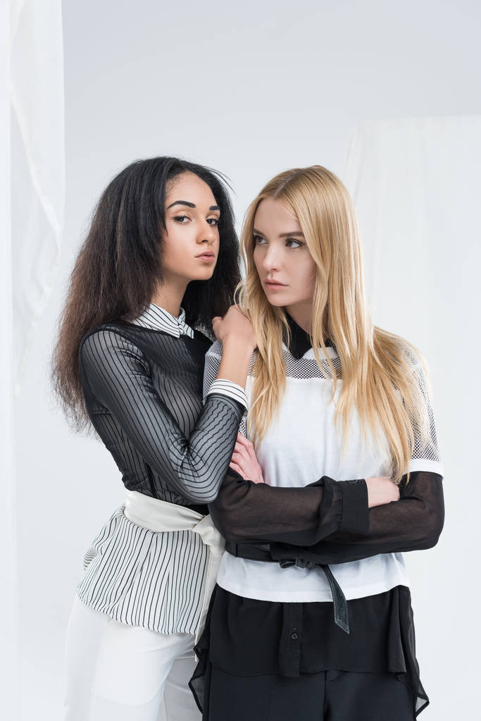 привлекательная многонациональная блондинка и брюнетка женщины в черно-белой одежде позируют изолированно на белом
 - Фото, изображение