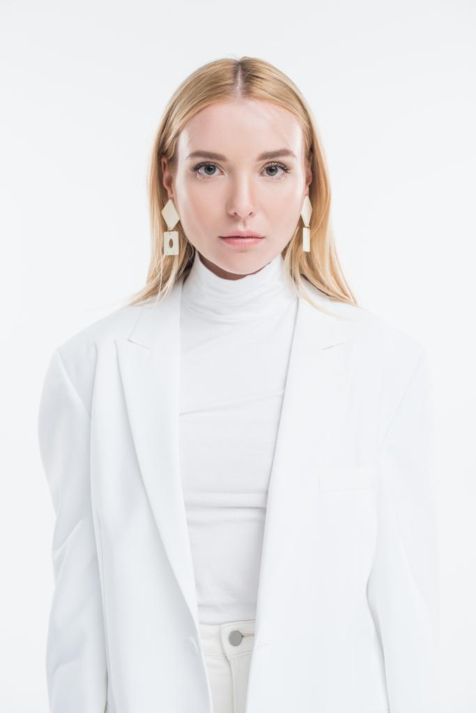портрет привабливої білої блондинки в модному білому одязі і сережках дивиться на камеру ізольовано на білому
 - Фото, зображення