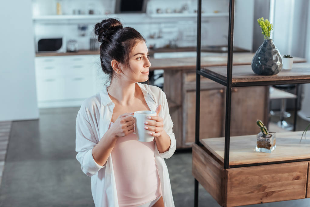 menina sorridente em camisa branca segurando xícara de café durante a manhã em casa
 - Foto, Imagem