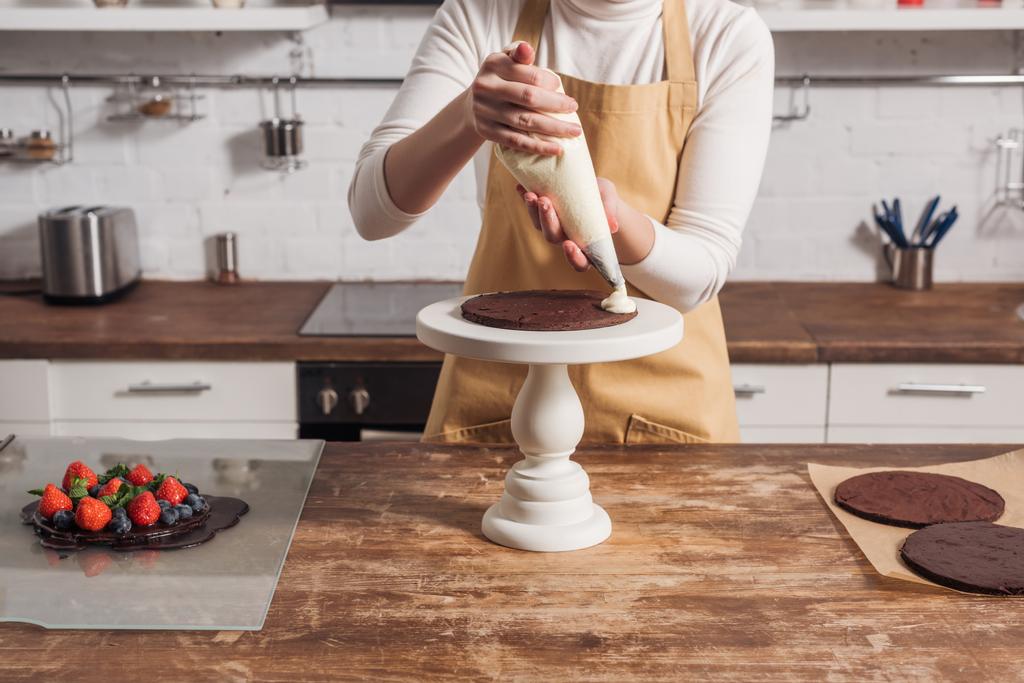 partial view of woman in apron decorating delicious homemade cake with cream    - Photo, Image