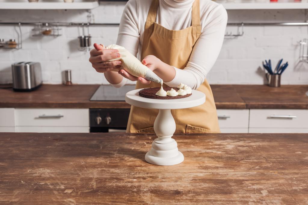 partial view of woman in apron decorating sweet homemade cake with cream   - Photo, Image
