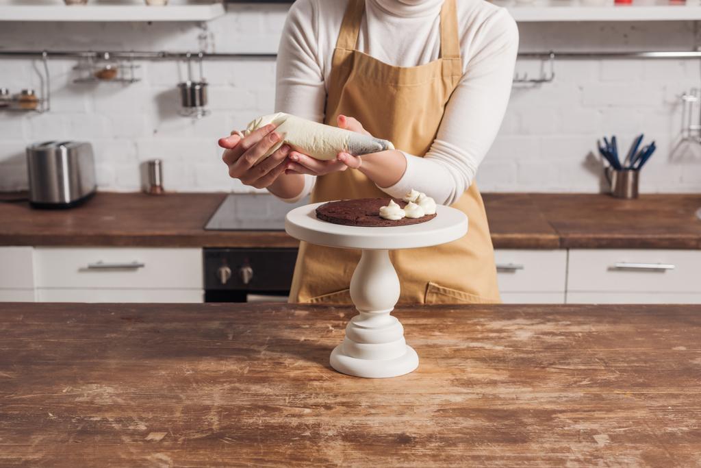 περικοπεί shot της γυναίκας στην ποδιά διακόσμηση γλυκό σπιτικό κέικ με κρέμα  - Φωτογραφία, εικόνα