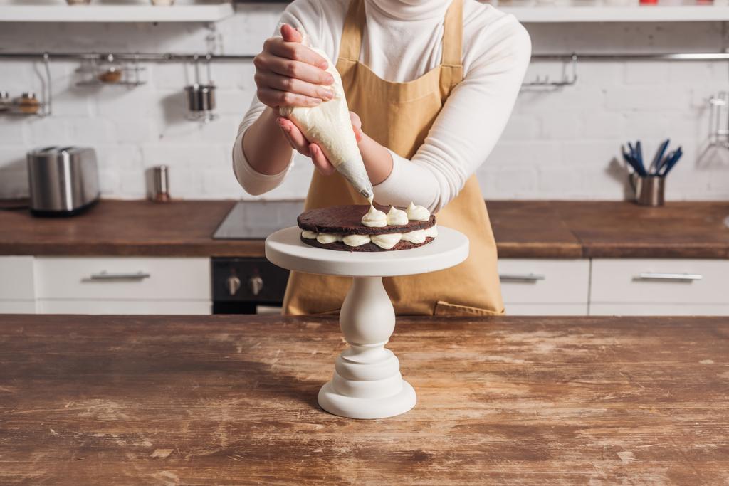 Mittelteil der Frau in Schürze dekoriert Gourmet-Kuchen mit Sahne    - Foto, Bild