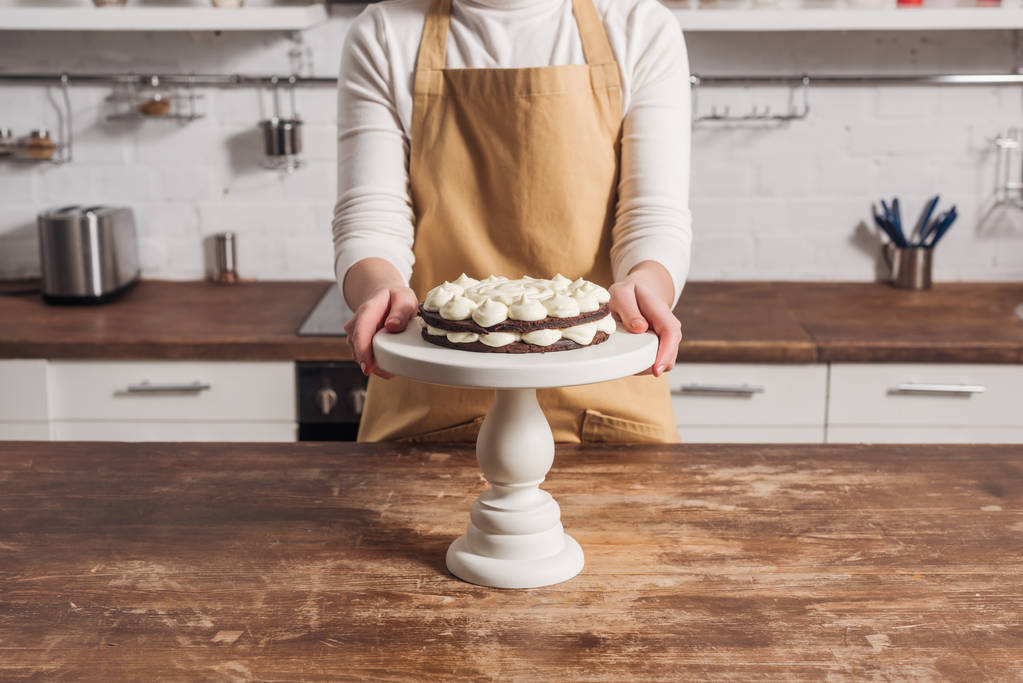 przycięte zdjęcie kobiety w fartuch gotowanie pyszne słodkie ciasto z kremem  - Zdjęcie, obraz
