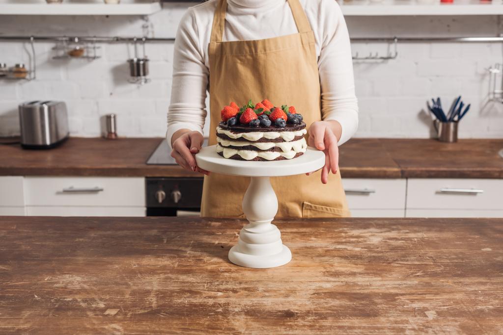 エプロン キッチンで果実とおいしいケーキを準備する女性のショットをトリミング - 写真・画像