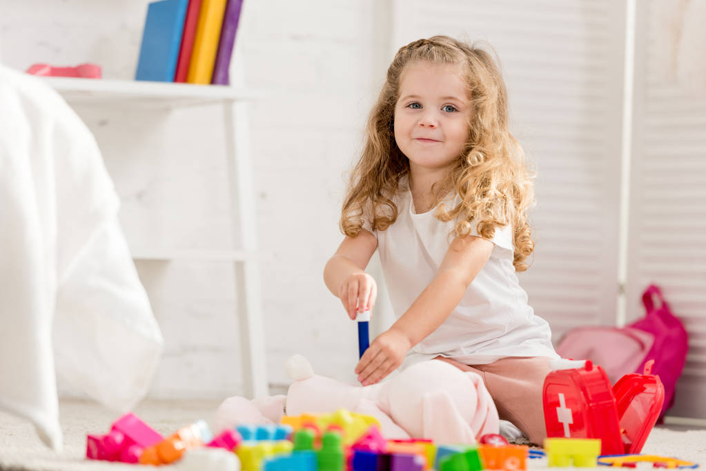 adorable kid examining rabbit toy with in children room and looking at camera - Photo, Image
