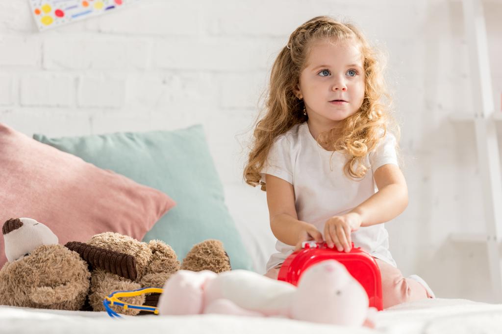 entzückendes Kind öffnet Verbandskasten, Kaninchenspielzeug auf dem Bett im Kinderzimmer - Foto, Bild