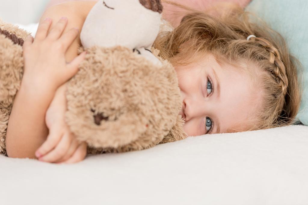 cheerful adorable kid hugging teddy bear on bed in children room - Photo, Image