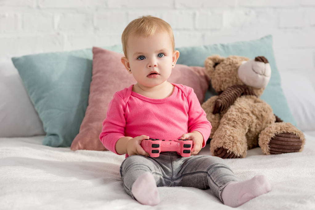 子供部屋のベッドの上のピンクのジョイスティックを保持しているピンクのシャツで愛らしい子 - 写真・画像