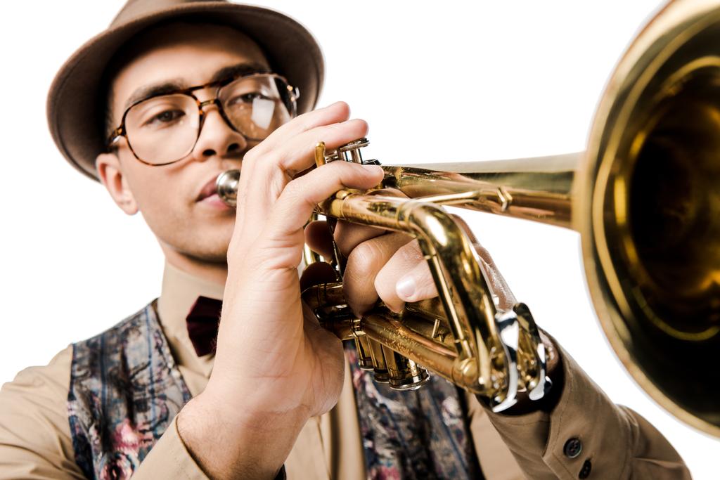 Nahaufnahme eines jungen Mannes gemischter Rasse mit stylischem Hut und Brille, der isoliert auf weißer Trompete spielt  - Foto, Bild