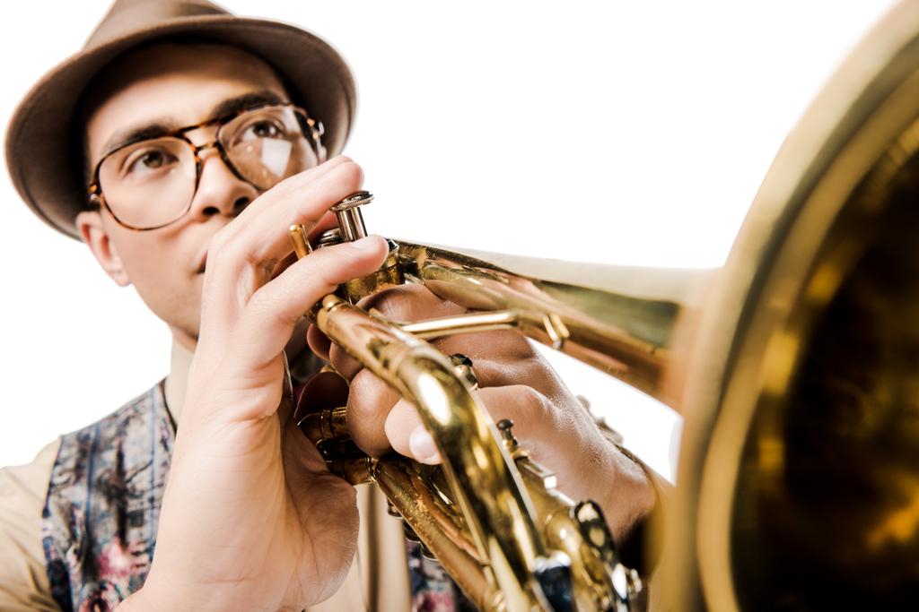selektiver Fokus eines männlichen Musikers gemischter Rasse mit stylischem Hut und Brille, der isoliert auf weißer Trompete spielt  - Foto, Bild