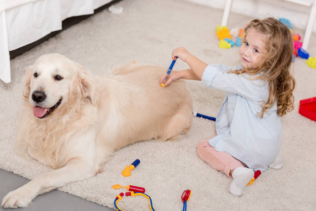 visão de alto ângulo de criança adorável fingindo veterinário e examinando golden retriever na sala de crianças
 - Foto, Imagem