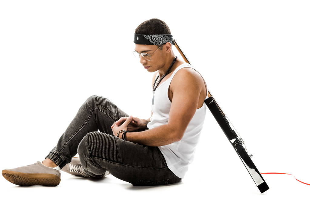 junger männlicher Rockmusiker sitzt mit schwarzer E-Gitarre auf dem Rücken isoliert auf weißem Boden - Foto, Bild
