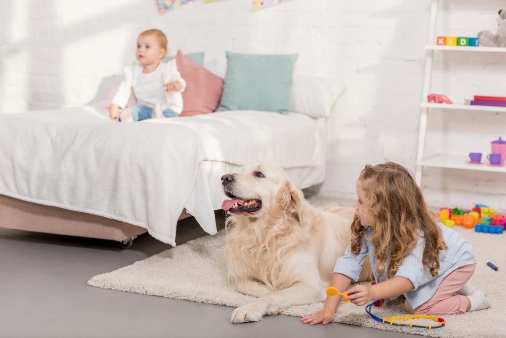 αξιολάτρευτο preschooler προσποιείται ότι κτηνίατρος και εξέταση golden retriever στο δωμάτιο παιδιών - Φωτογραφία, εικόνα