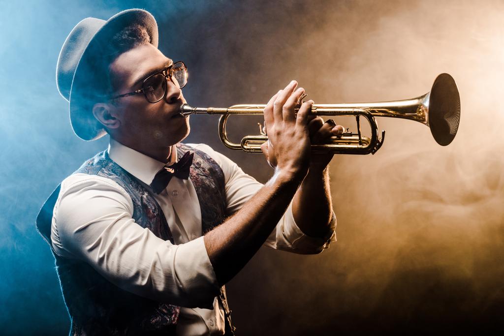 joven jazzman tocando la trompeta en el escenario con iluminación dramática y humo
 - Foto, Imagen
