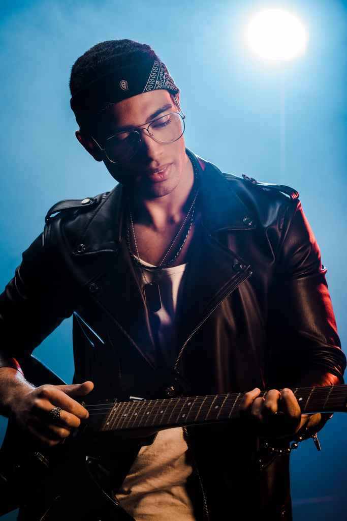 focused male rock star in leather jacket performing on electric guitar on stage with smoke and dramatic lighting  - Photo, Image